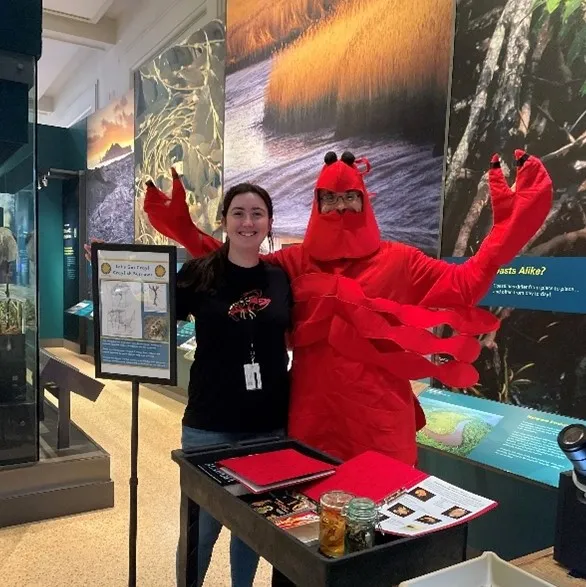 A woman and a man in a crayfish costume posing behind a public outreach display at the Natural History Museum